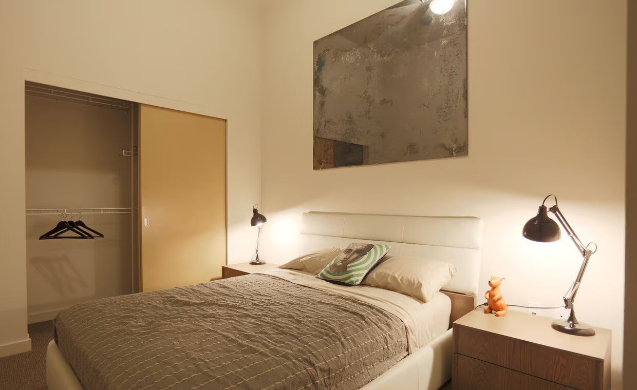A bedroom with a bed , nightstand , lamp and mirror on the wall.