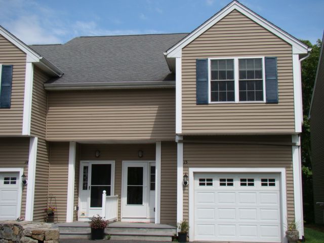 A tan house with a white garage door and black shutters