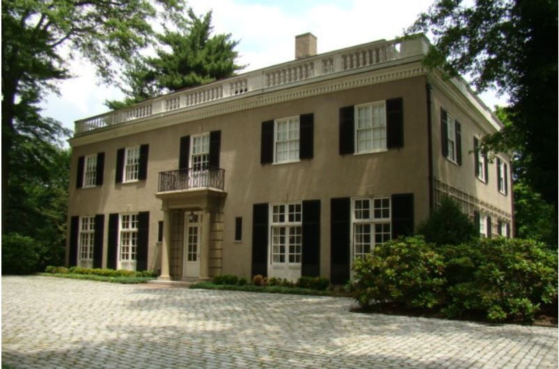 A large house with black shutters is surrounded by trees