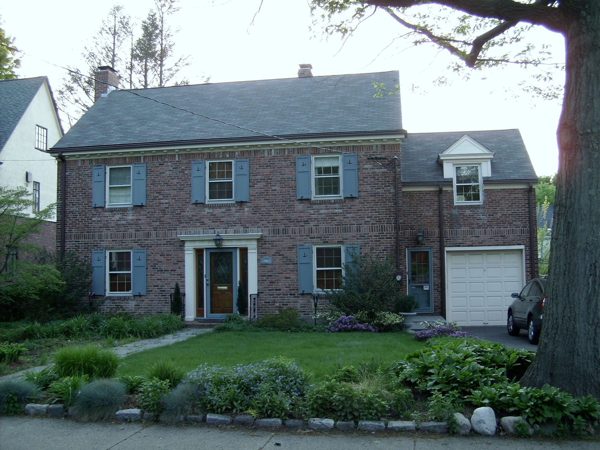 A brick house with blue shutters and a car parked in front of it