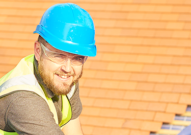 a man wearing a blue hard hat and safety glasses is working on a roof .