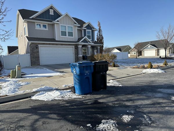 Two trash cans are sitting on the side of the road in front of a house.