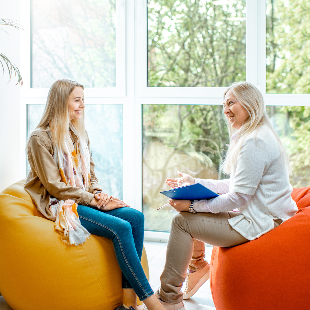 A professional session where two people sit in colorful beanbag chairs by a window, discussing notes on a clipboard.