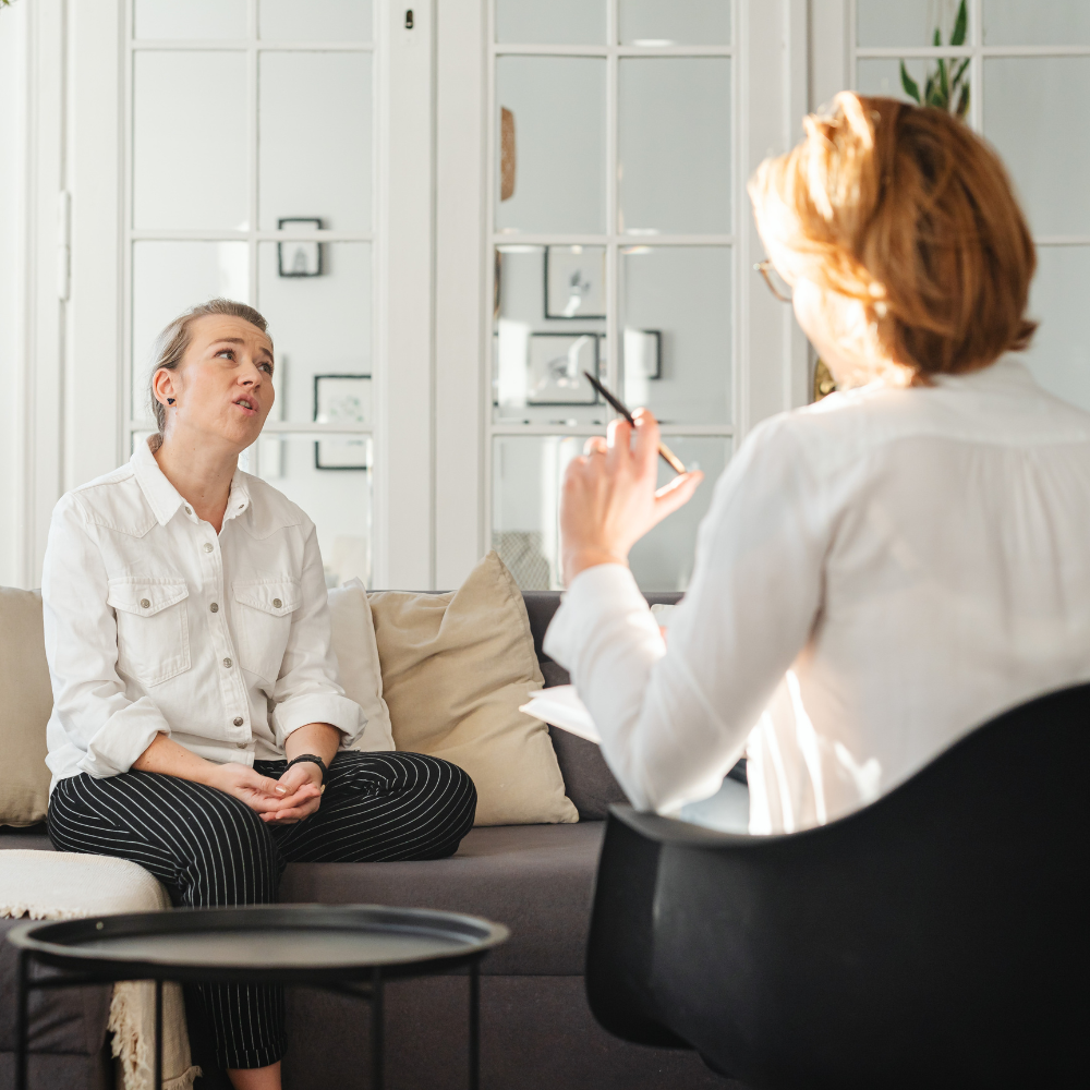 A professional session where one person sits on a sofa talking to another individual who is taking notes.