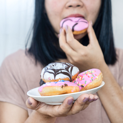 A person holds a plate of assorted colorful, frosted donuts while eating a pink one.