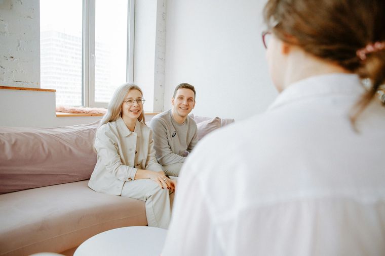 A couple sits together on a couch, facing an unseen person, during what appears to be a professional consultation.