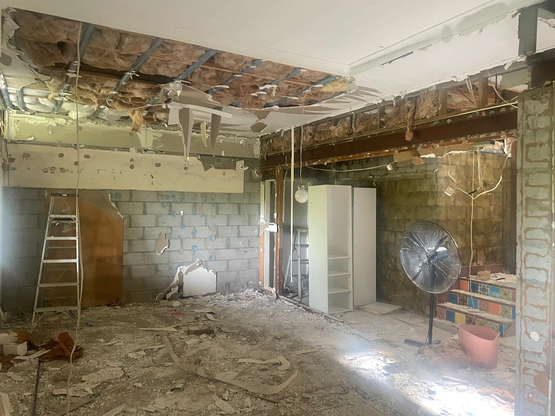 Basement renovation in progress: concrete block walls, exposed ceiling beams, doorway, concrete floor, insulation visible.