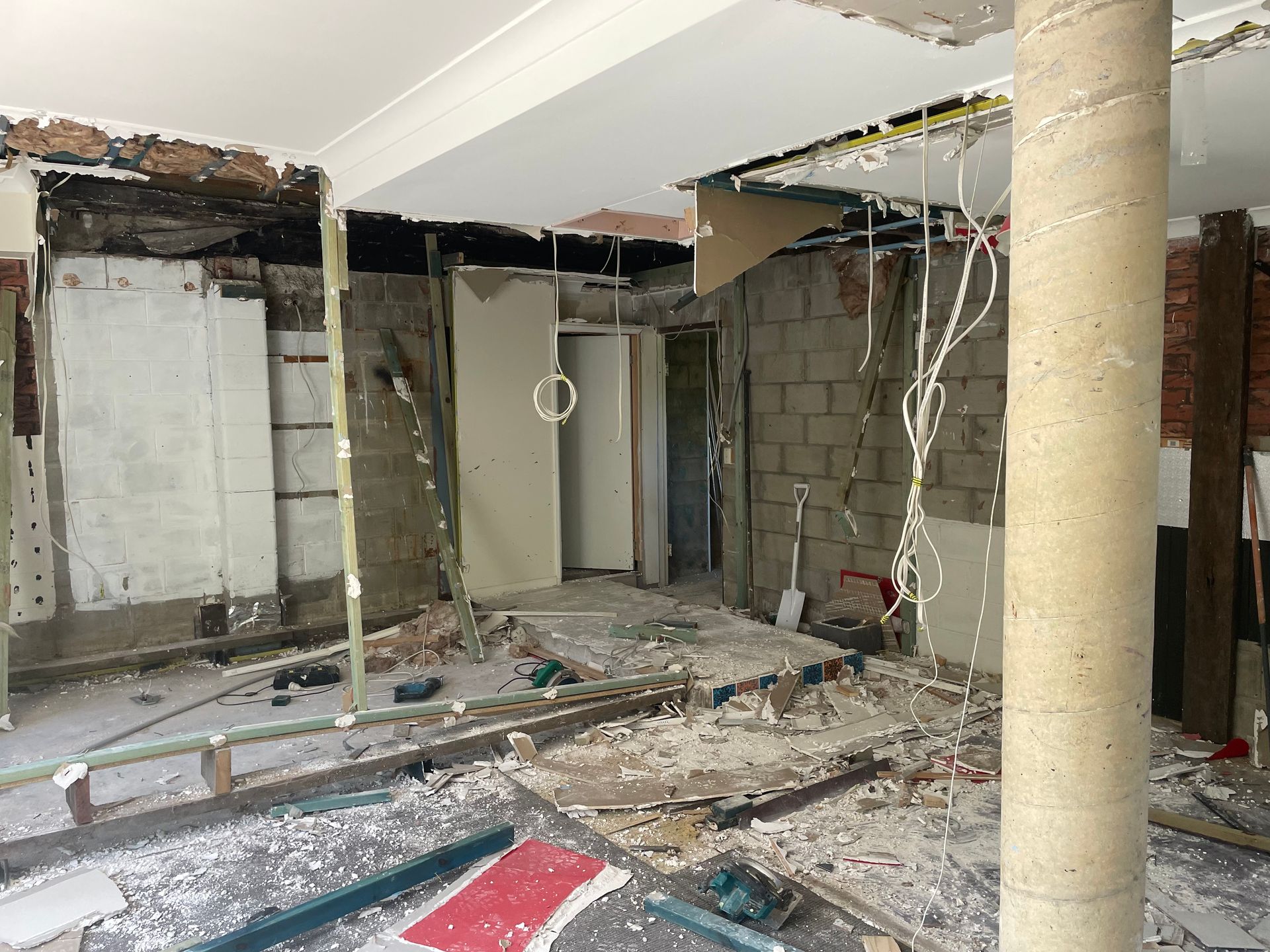 Interior room under construction, exposed brick and electrical wiring. Debris covers the floor.