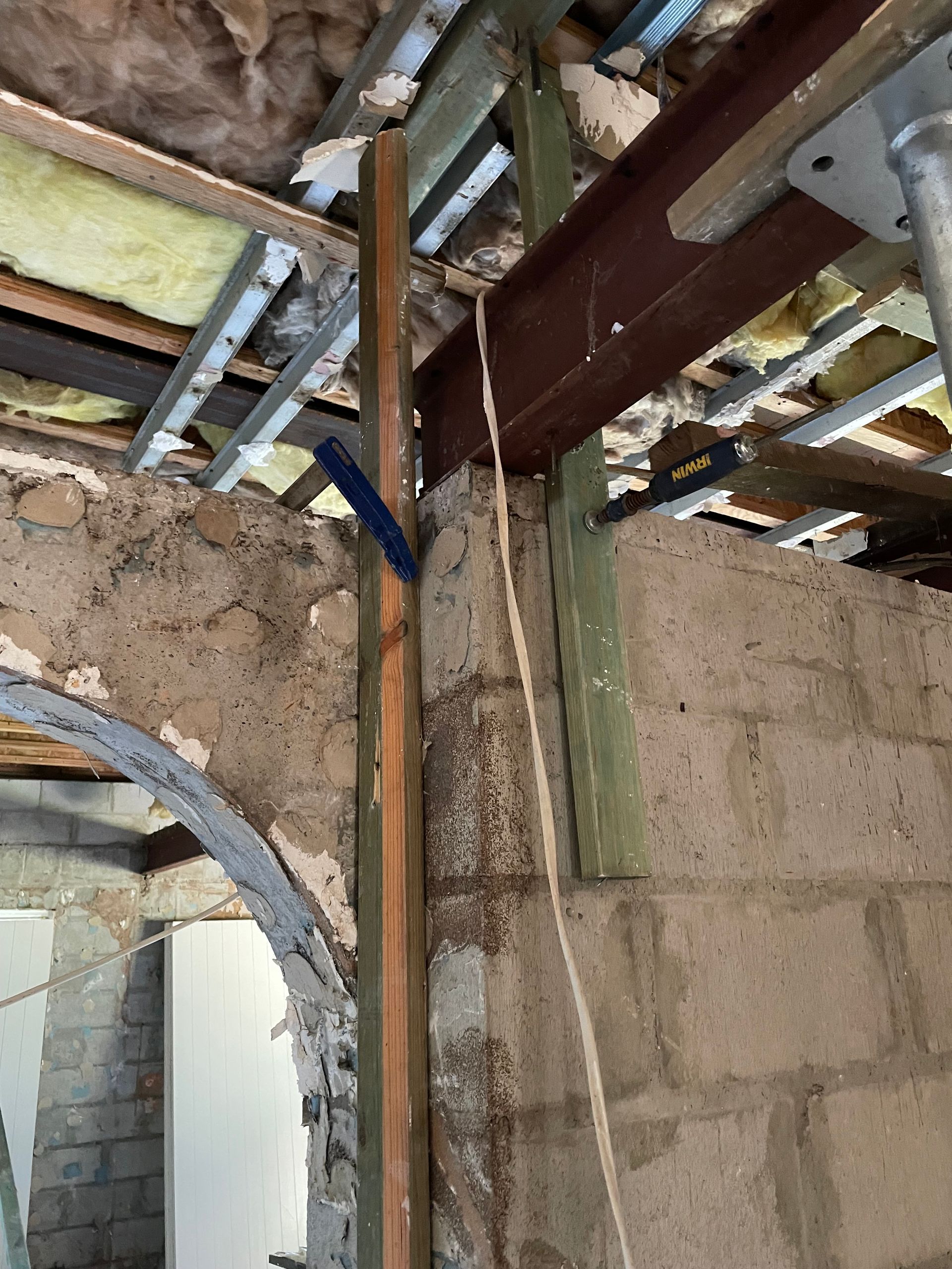 Room under renovation with exposed ceiling, debris, and lumber leaning against a cinder block wall.