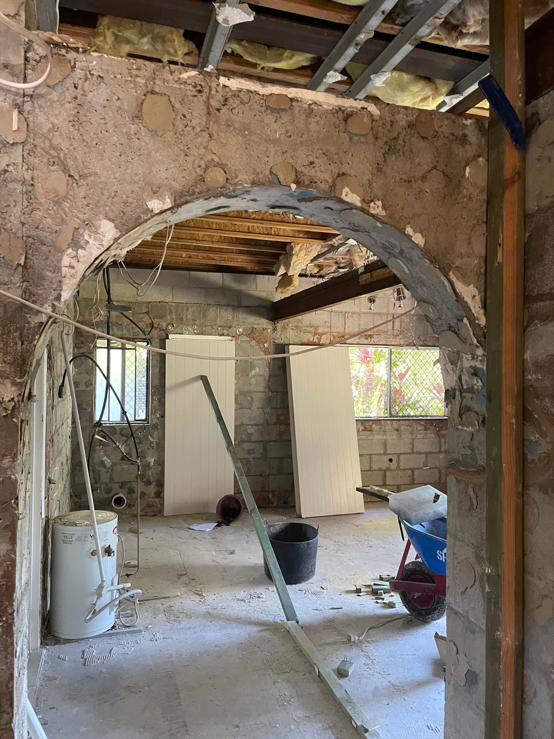 Interior undergoing renovation with a metal beam supported by temporary posts. Construction debris and a ladder are present.
