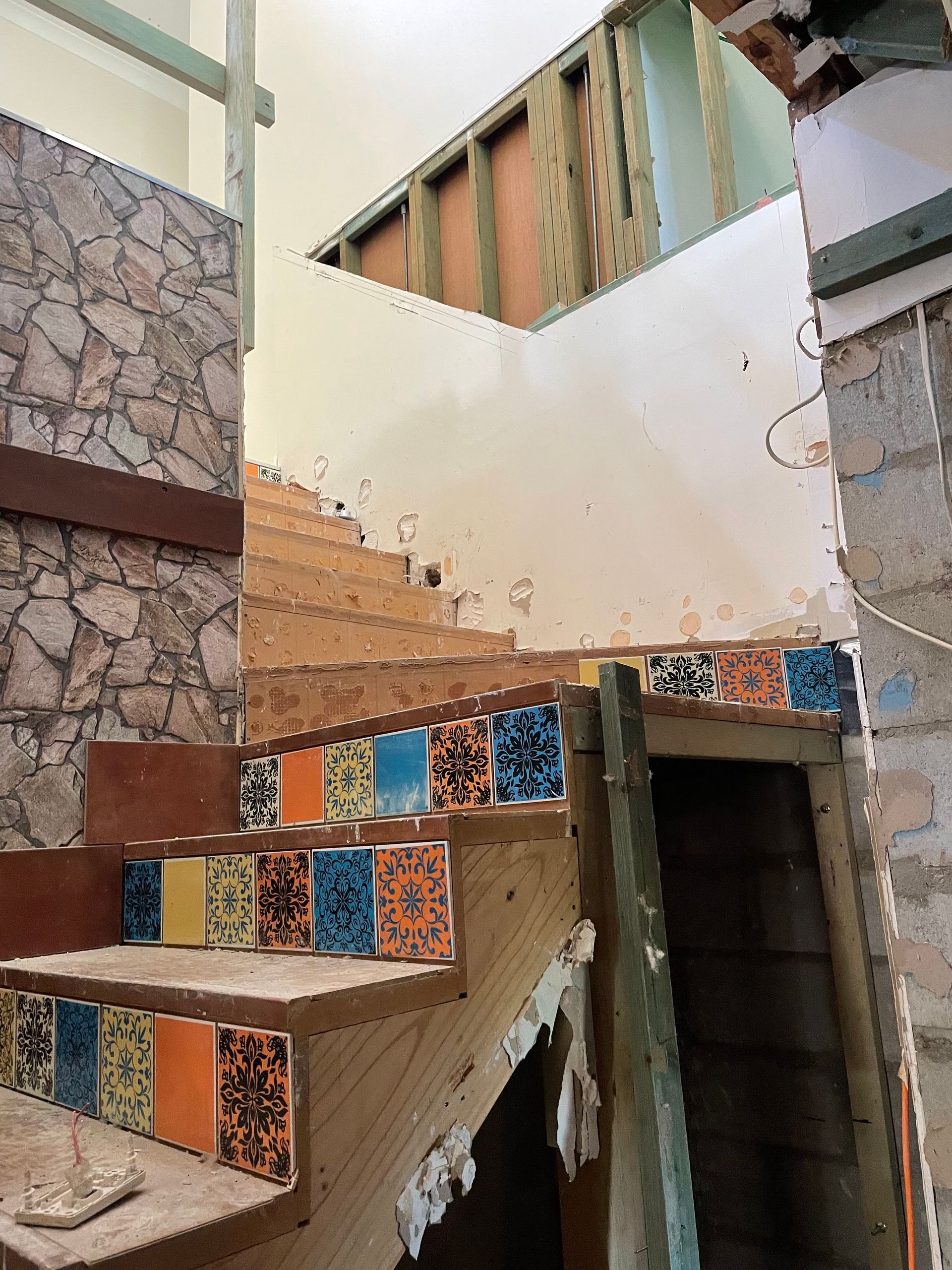 Staircase under renovation with decorative tiles on the steps. Wall features stone and drywall.