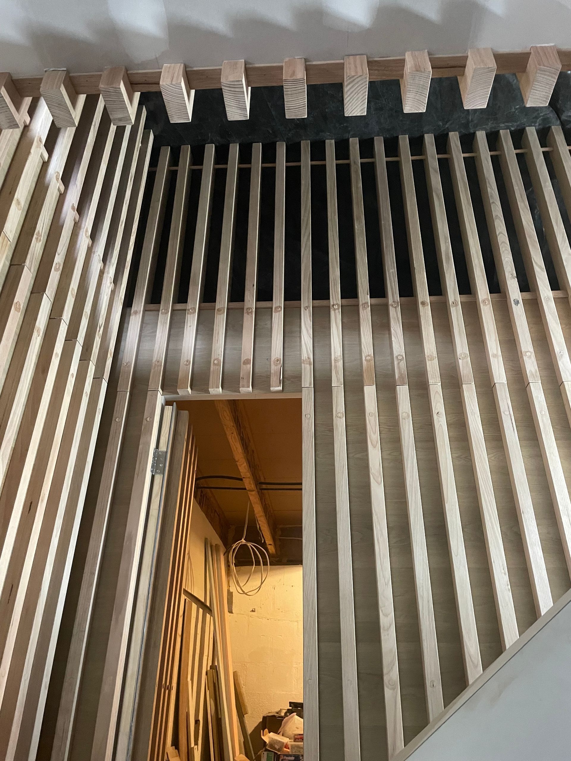 Wooden slat wall construction, partially framing a doorway and stairs.
