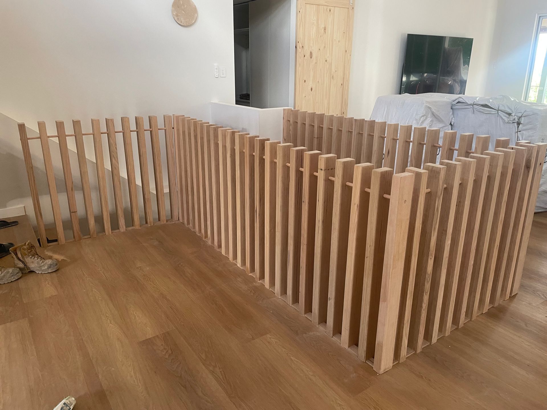 A wooden fence structure with vertical slats, set on a wood floor, in an indoor setting.