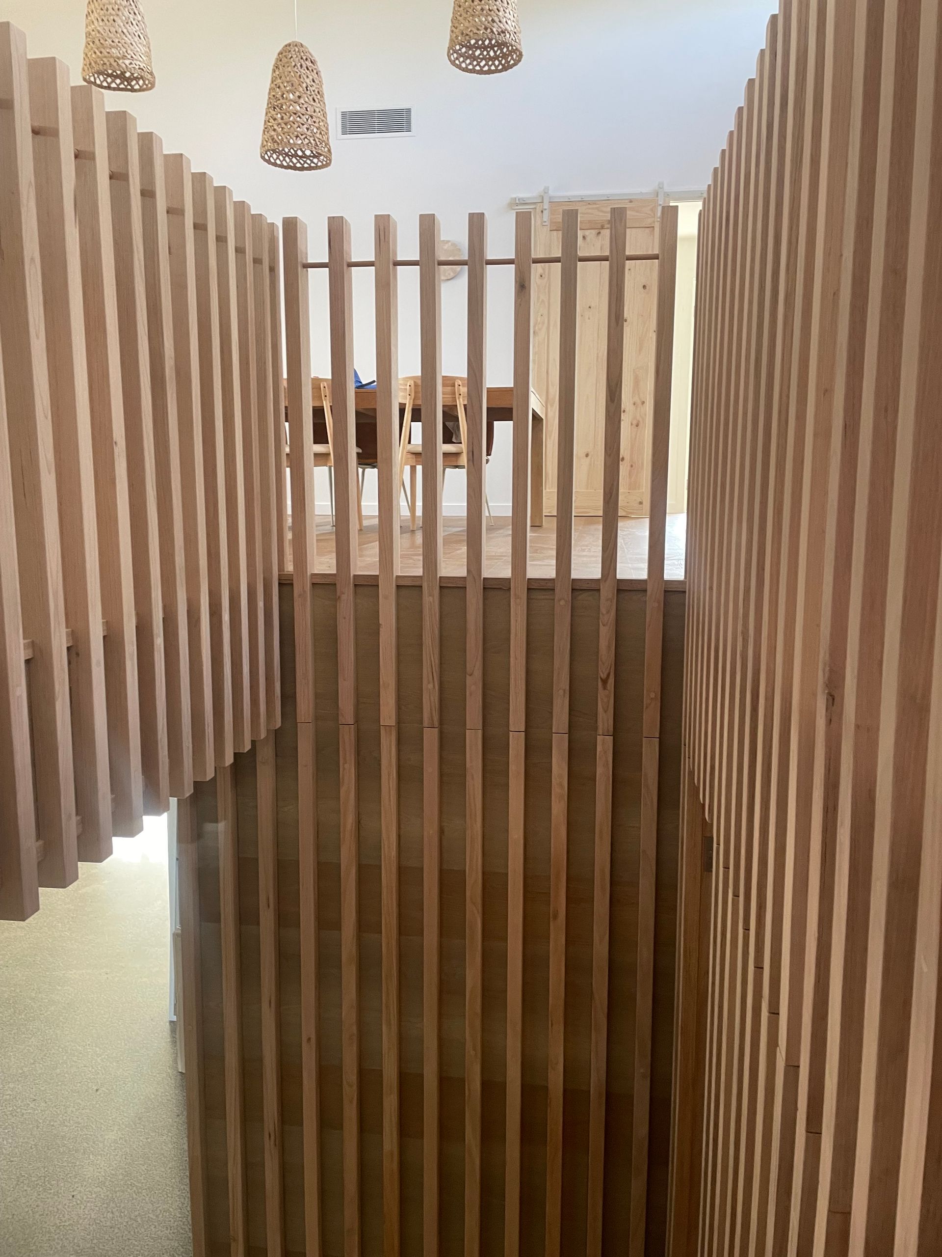 Wooden slat fence inside a building with light wood floors and walls.