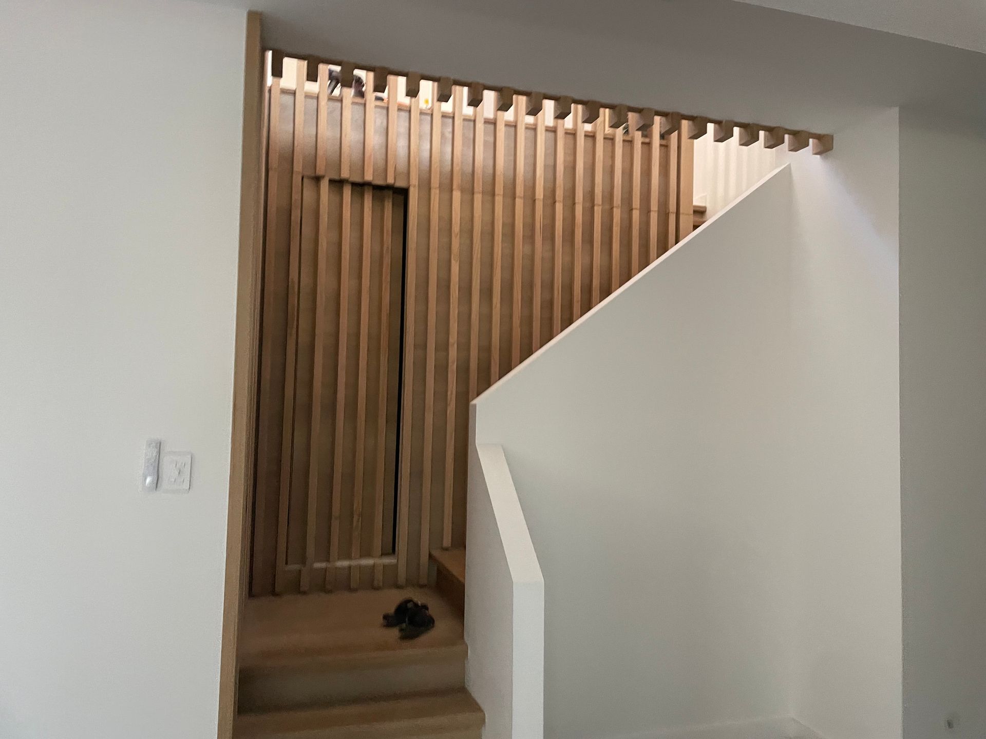 Wooden slat wall and door, white staircase and walls, interior shot.
