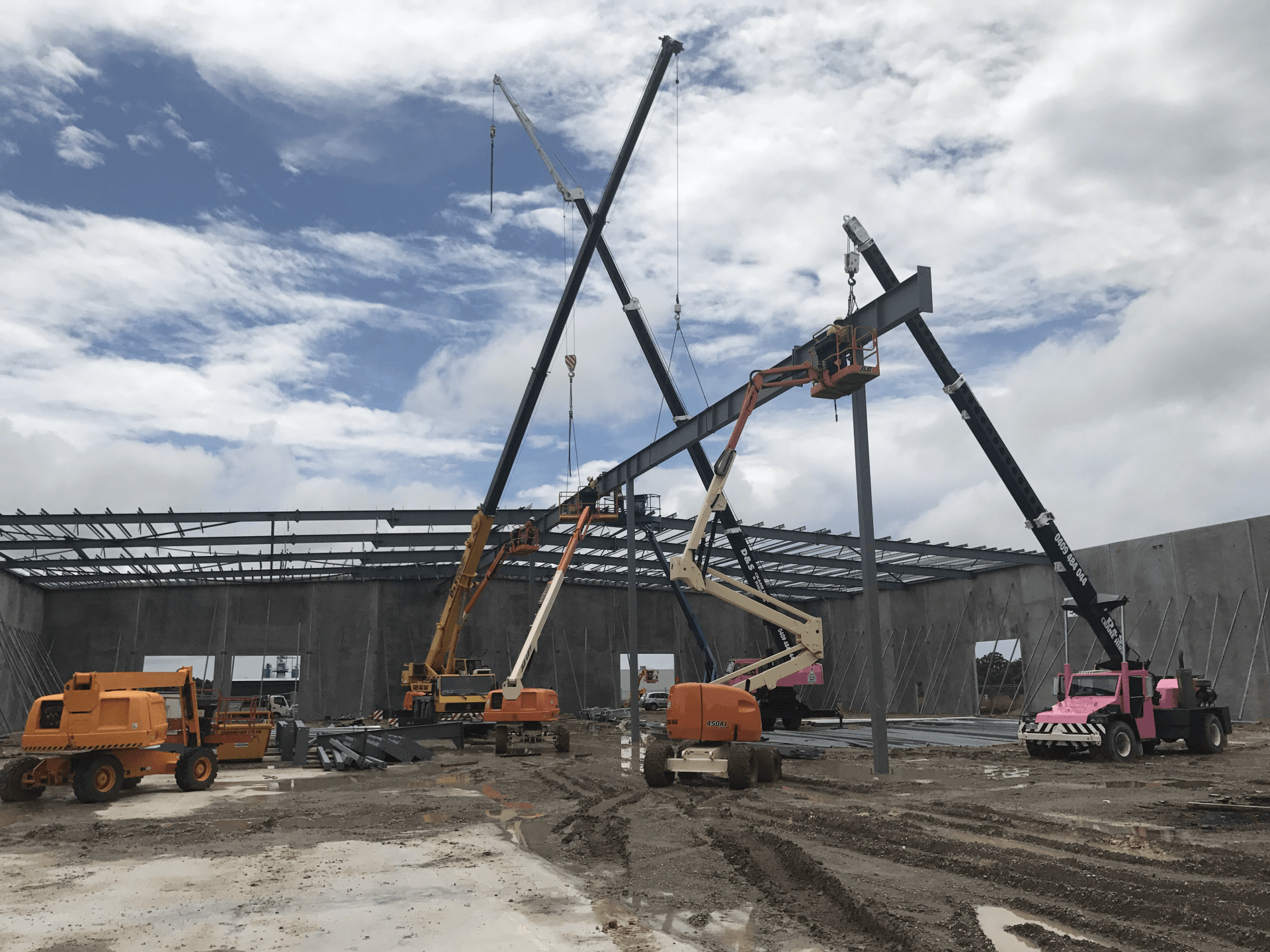 cranes and access equipment lifting structural steel on a commercial construction site