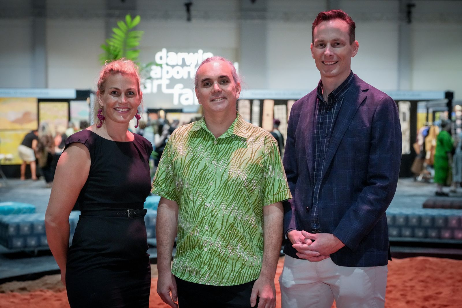 One lady and two men posing for a photo against the backdrop of an art festival. 