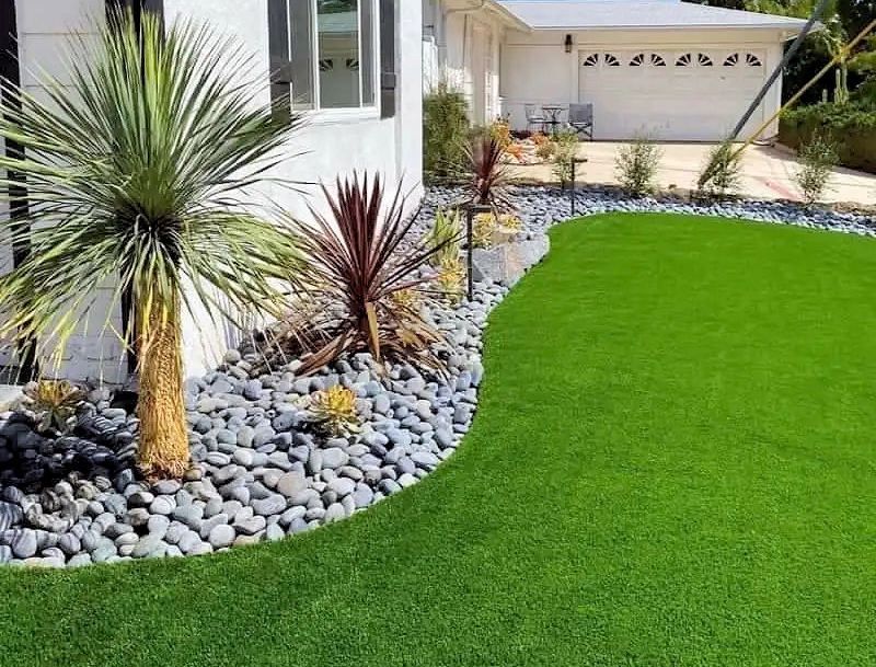 A house exterior with vibrant green artificial turf, a rock garden, and a palm tree.