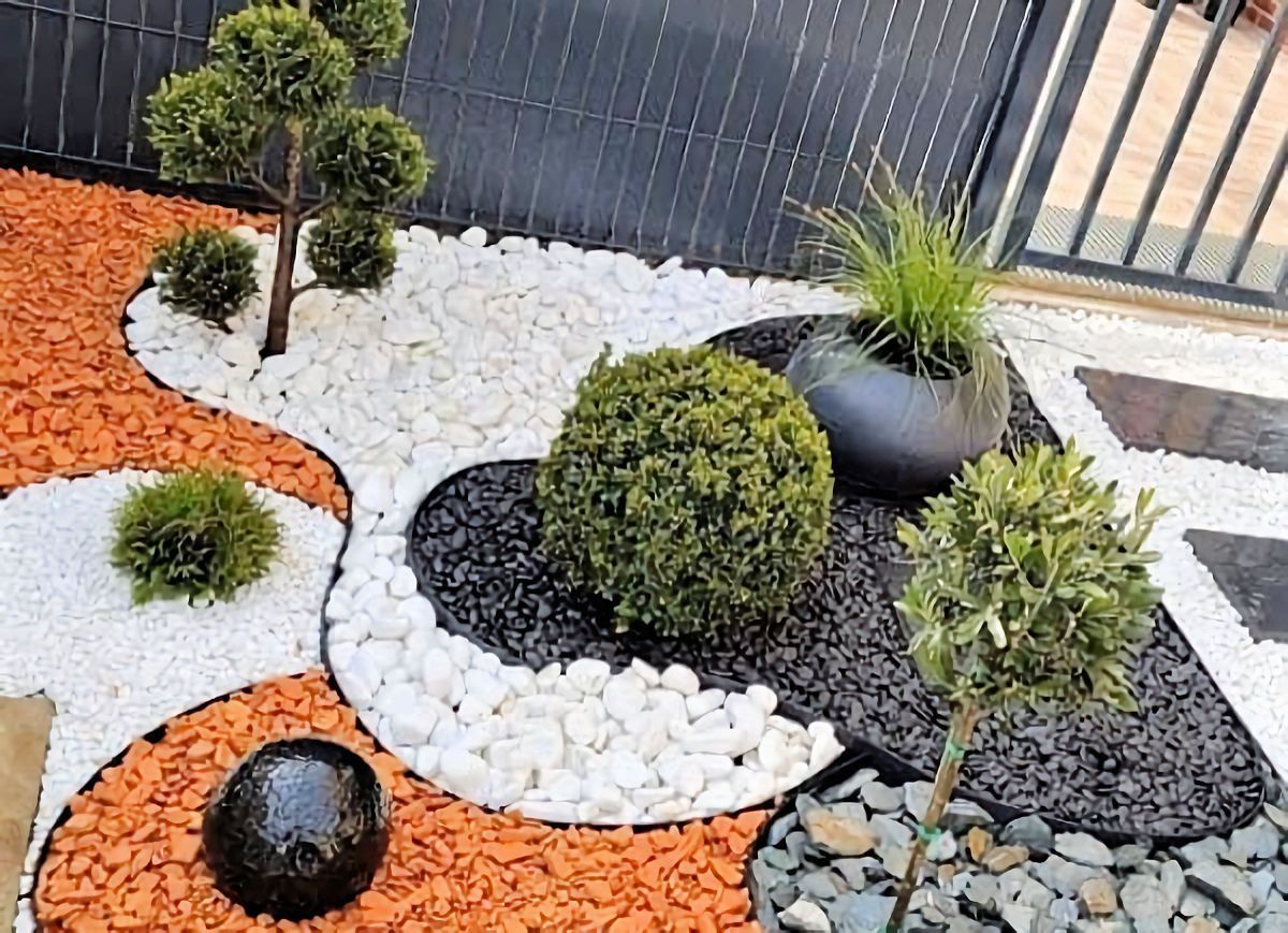 Decorative garden bed with orange, white, and black stones, and green shrubs.