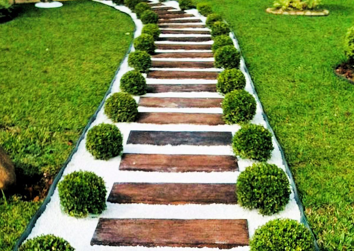 Wooden stepping stones path through white rock, bordered by green grass and rounded green bushes.