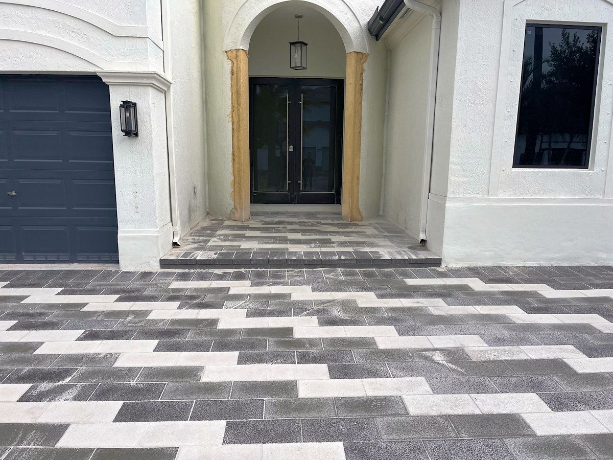 A black and white driveway in front of a white house with a black garage door.