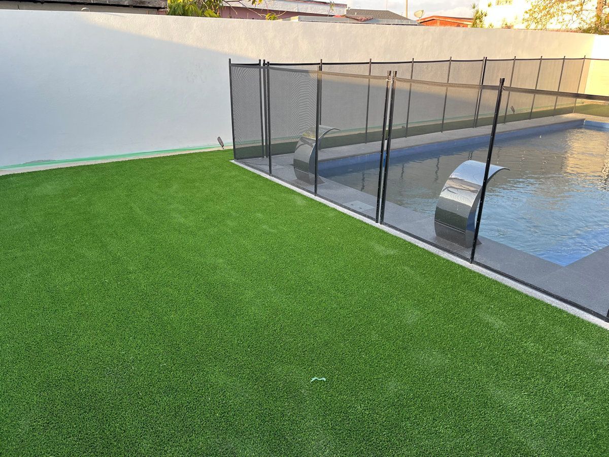 A swimming pool surrounded by a fence and a lush green lawn.