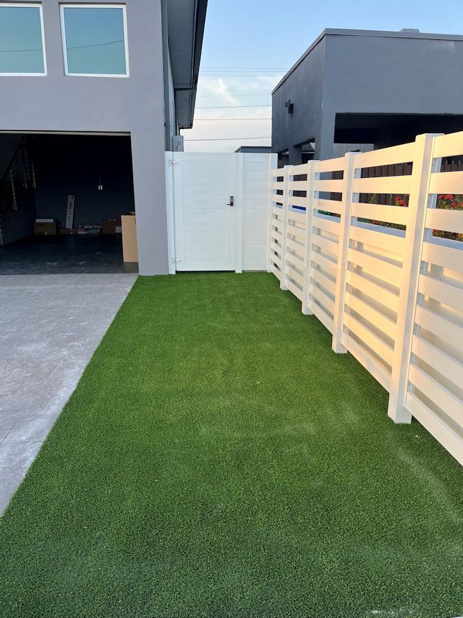 A white fence surrounds a lush green lawn in front of a house.