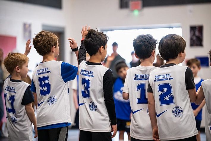 Youth hockey players in white jerseys huddle on the rink with numbers visible on their backs.