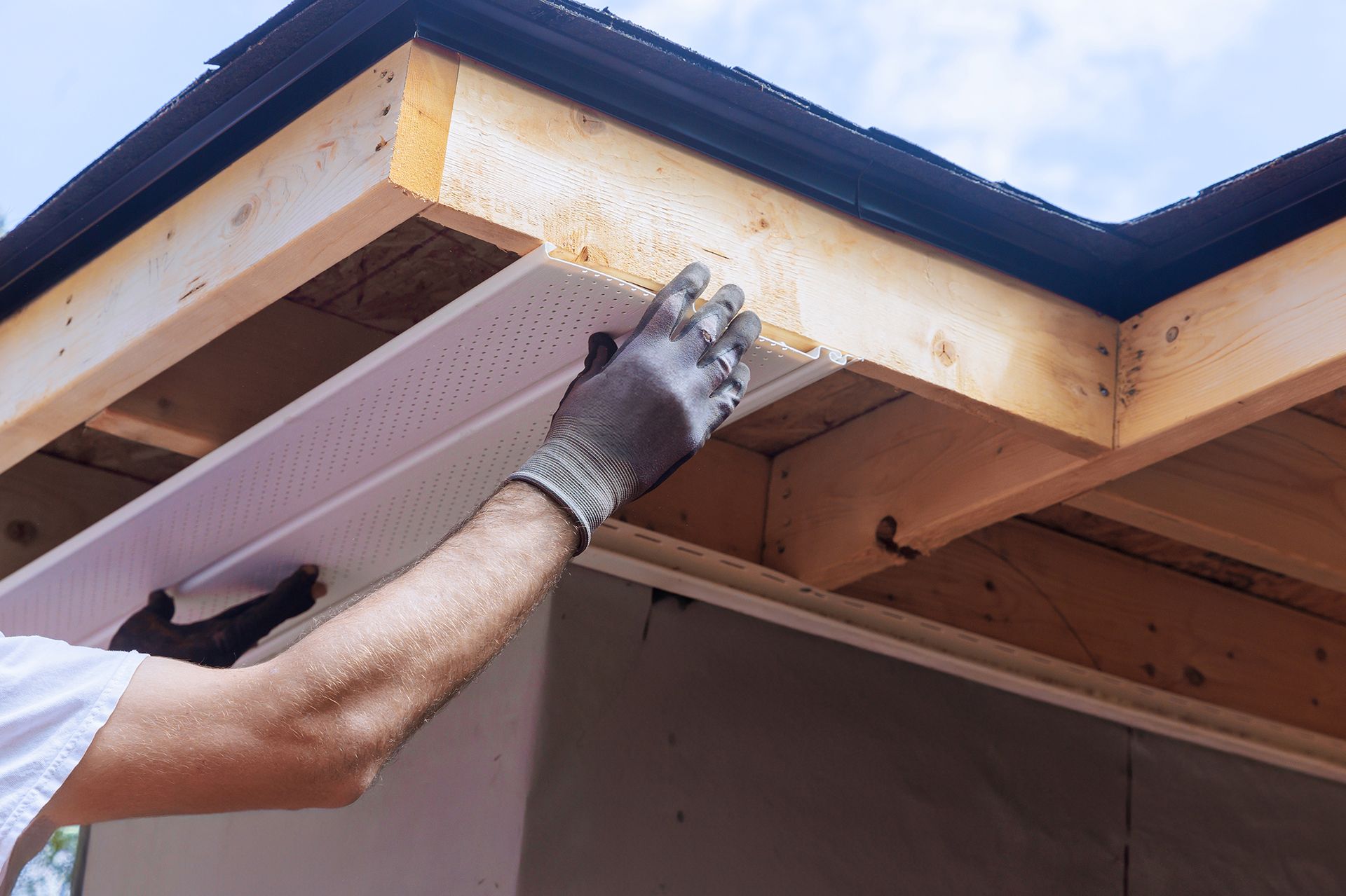 Person installing soffit panel on a building's overhang, wearing gloves.
