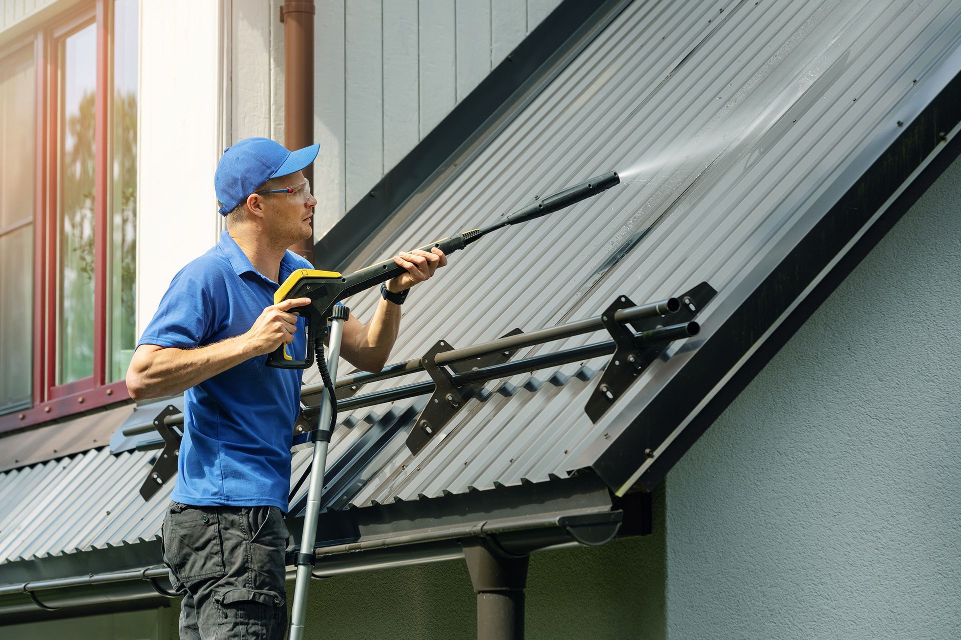 Man power washing a metal roof on a house