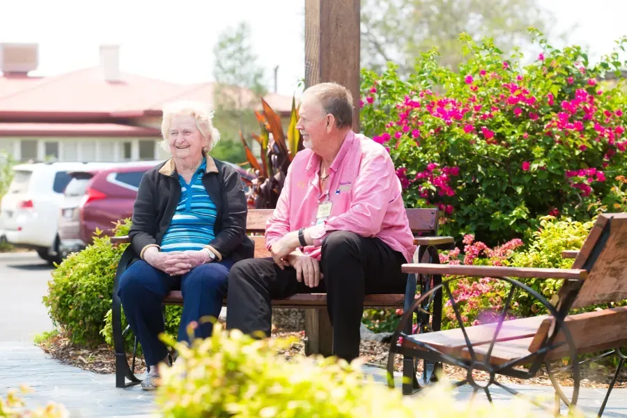 A man and a woman are at Beauaraba Living, they are sitting on a bench talking to each other.