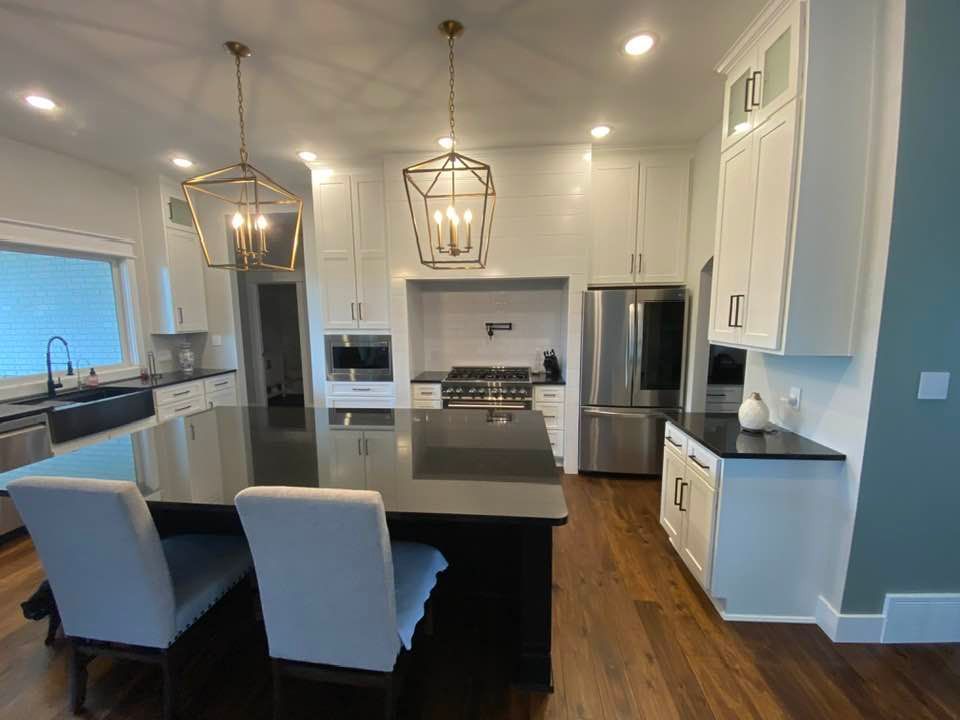 A kitchen with white cabinets , black counter tops , stainless steel appliances and a large island.