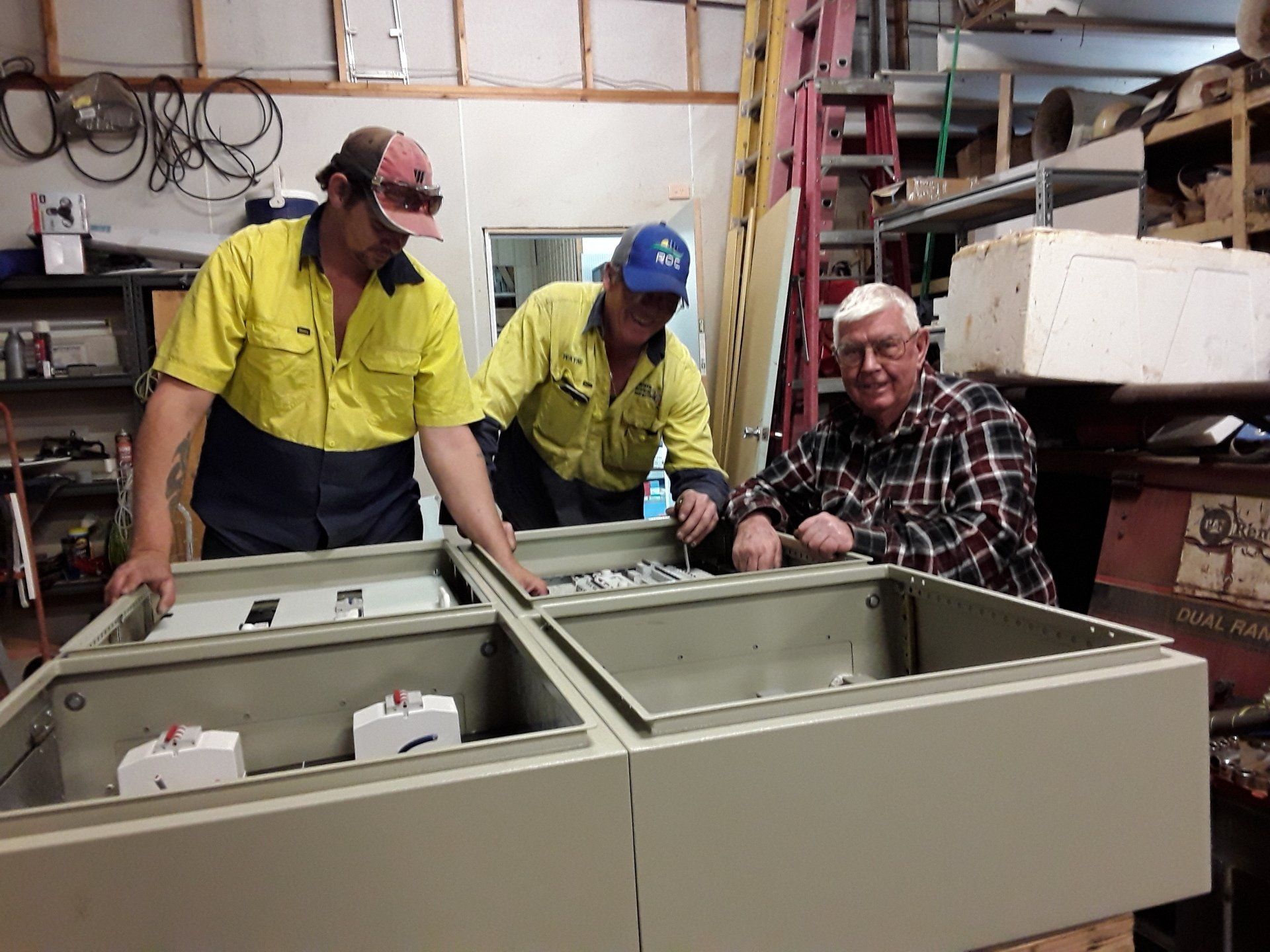 Three men are working on electrical boxes.