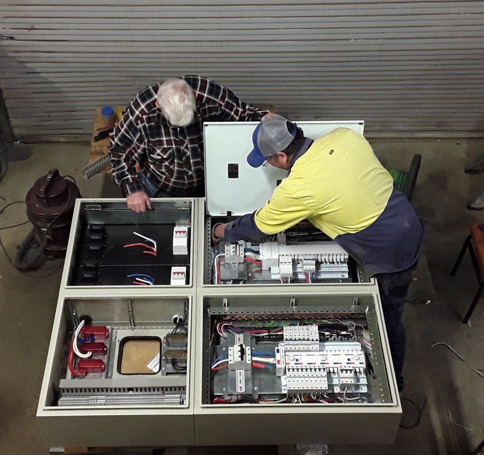 Two men are working on electrical boxes.