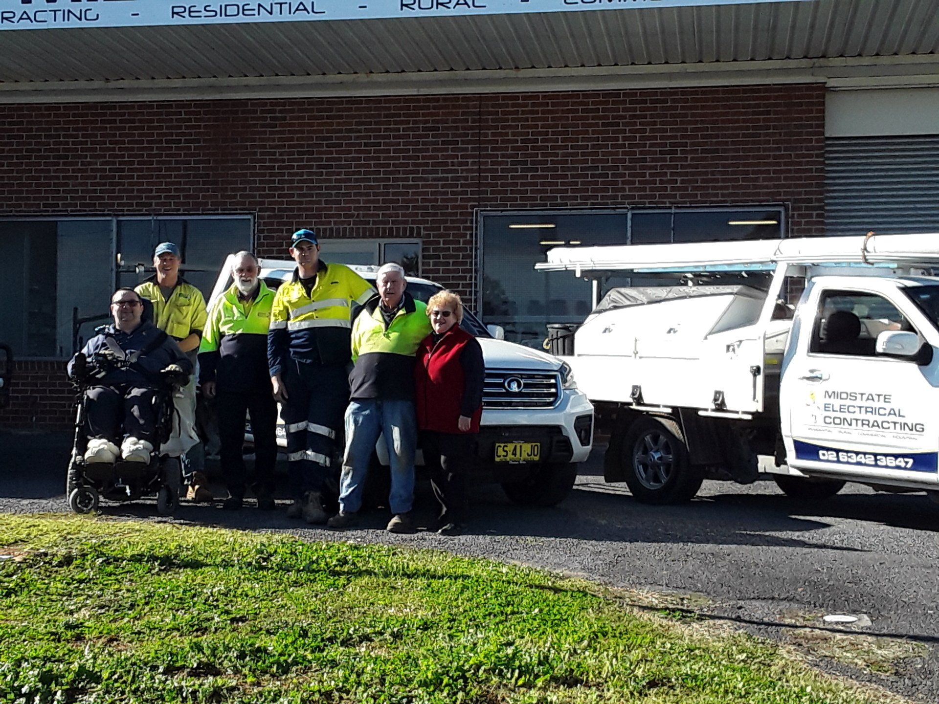 A group of people are posing for a picture in front of a Midstate Electrical Contracting building.
