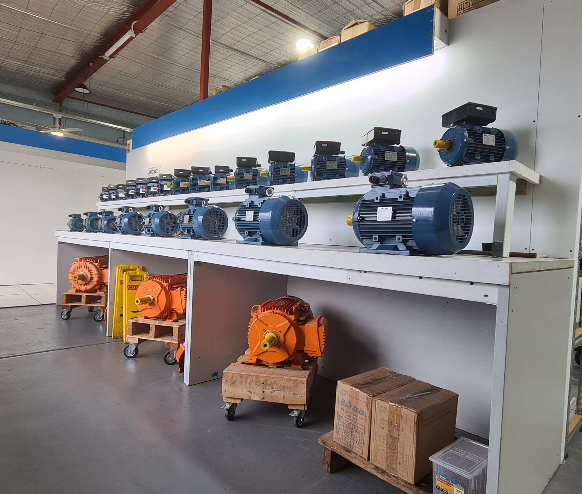 A row of black, blue, and orange electric motors sitting on top of a shelf.