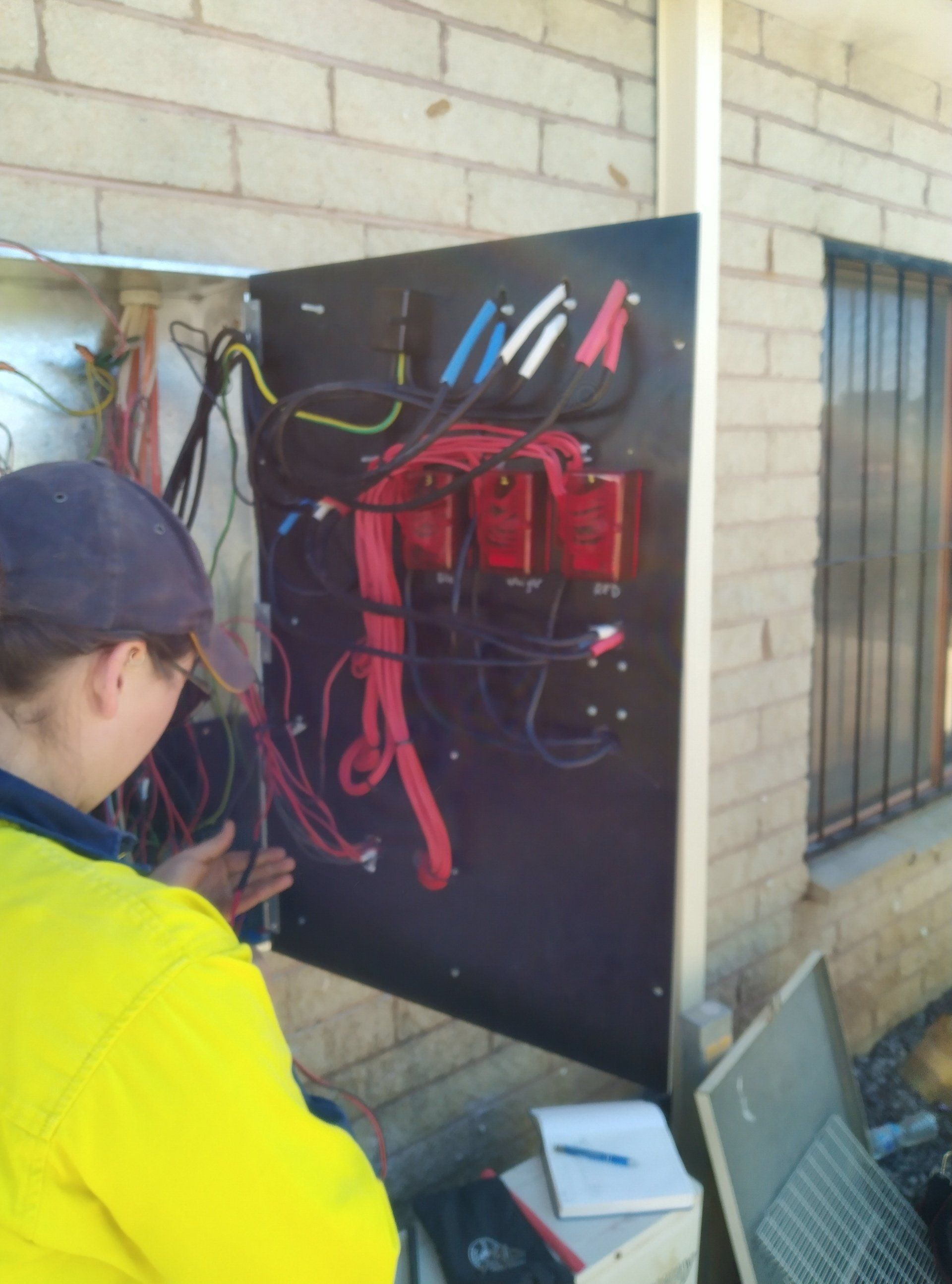 A man in a yellow jacket working on an electrical panel.