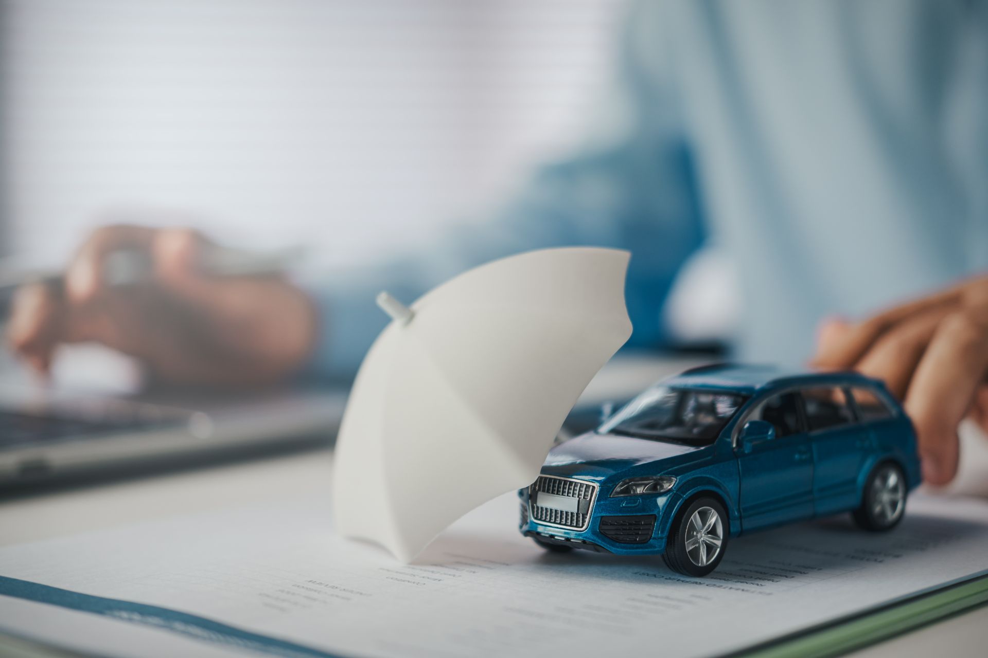 Small toy SUV protected by a umbrella on top of an open document, symbolizing car insurance or vehicle protection Small toy SUV protected by a umbrella on top of an open document, symbolizing car insurance or vehicle protection