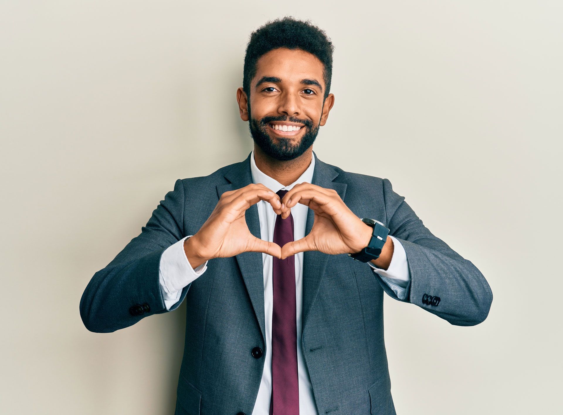 Man in suit makes heart shape with hands, smiling.