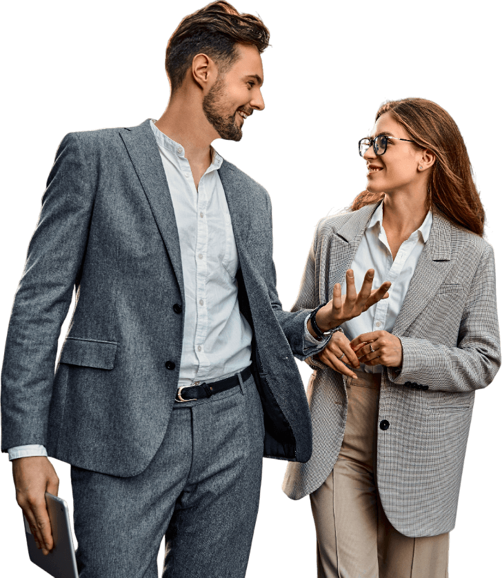 A man and woman in business attire smiling and talking. The man holds a tablet and the woman gestures with her hand.