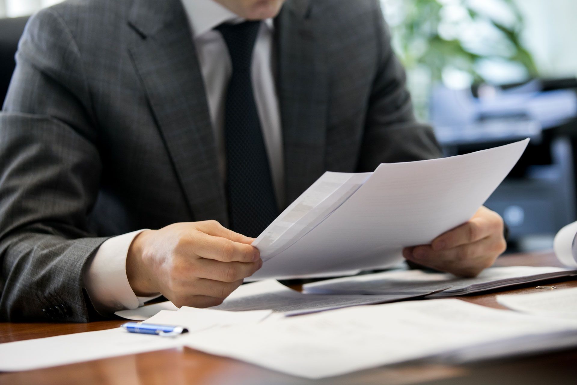 Man in a suit, reviewing papers at a desk in an office setting.