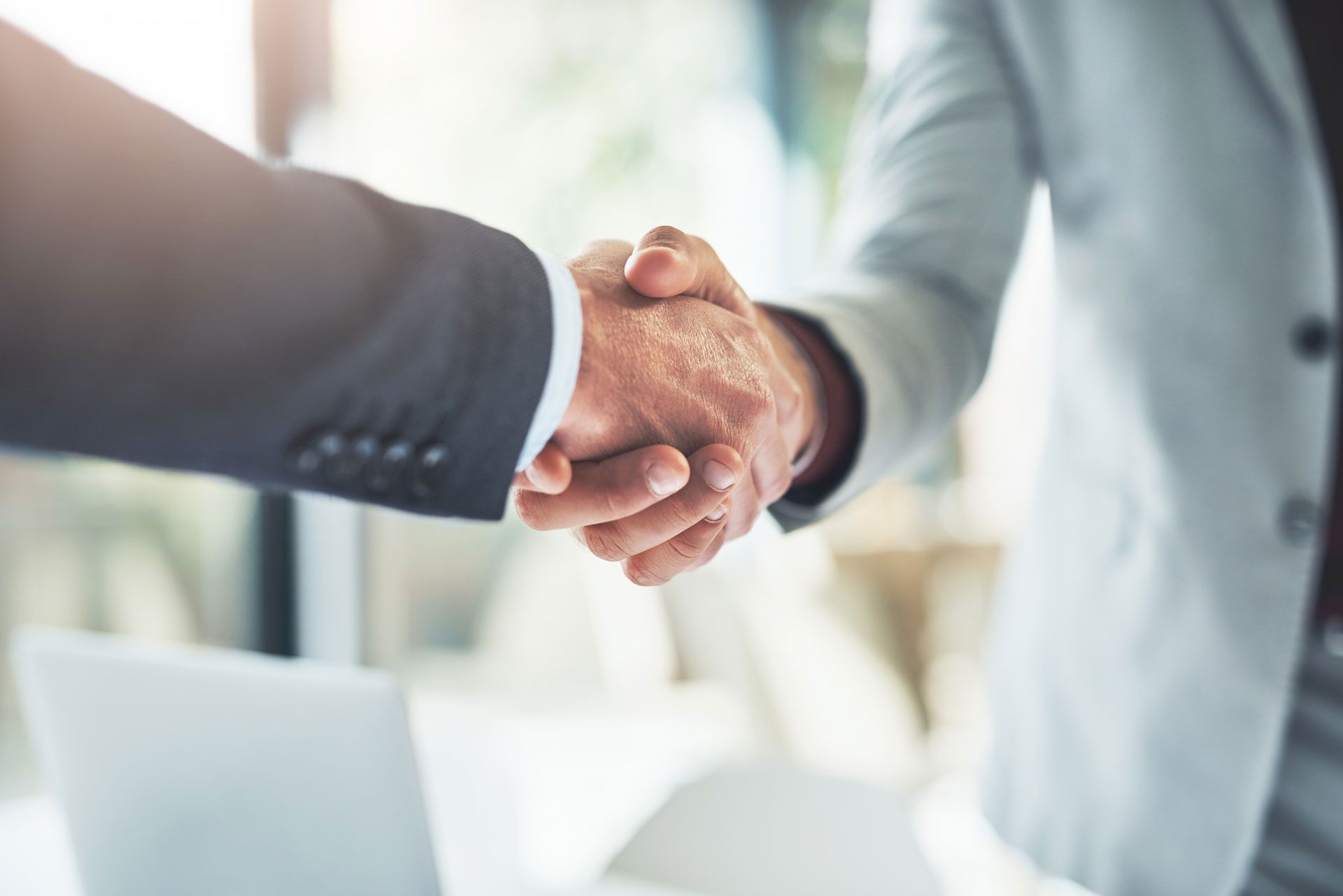 Two people in business suits shaking hands, symbolizing agreement or partnership. Blurred office setting.