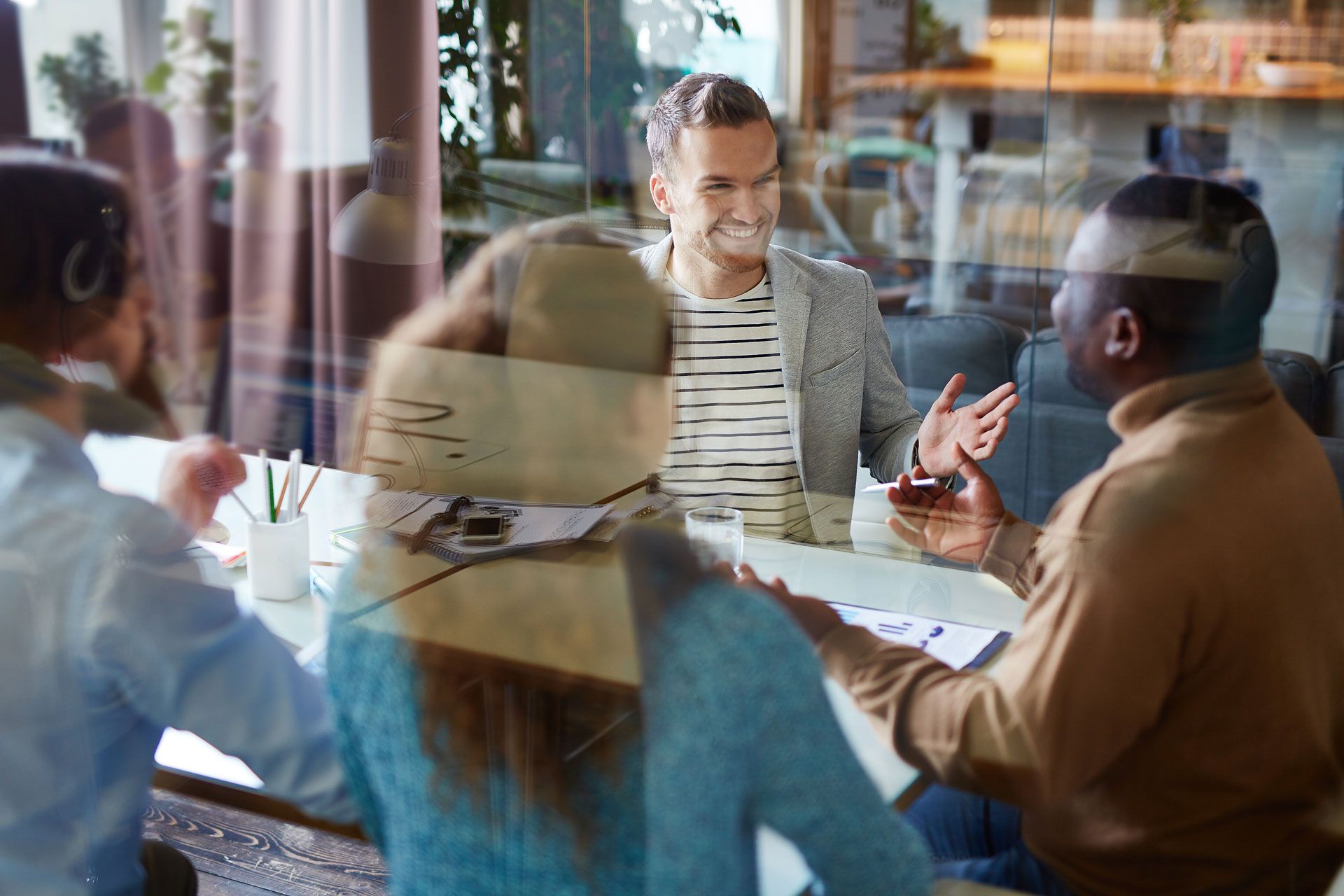 Business meeting in a bright office space. Four people seated at a table, engaged in conversation.