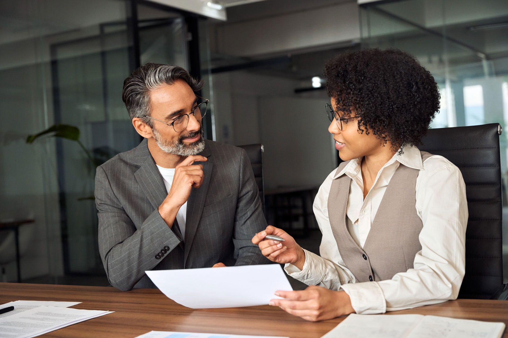 Two people in business attire reviewing documents at an office table.