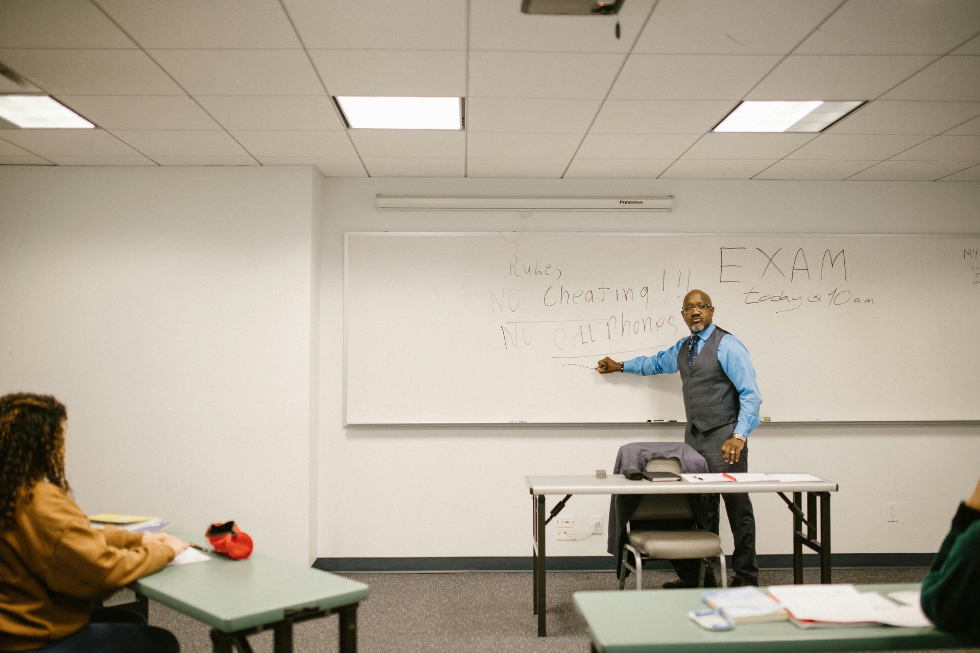 A man is standing in front of a whiteboard in a classroom.