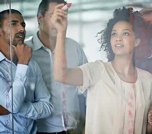 A group of people are writing on a glass wall finding a solution to a challenging client need