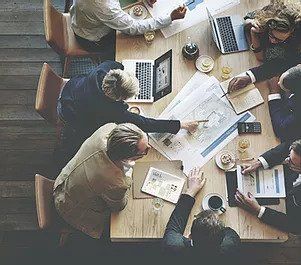 A group of people are sitting around a table having a meeting and collaborating with client.