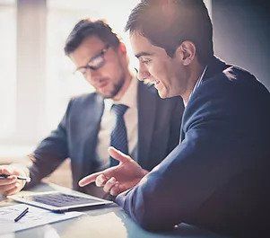 Two men are sitting at a table looking at a laptop working to get job done efficiently