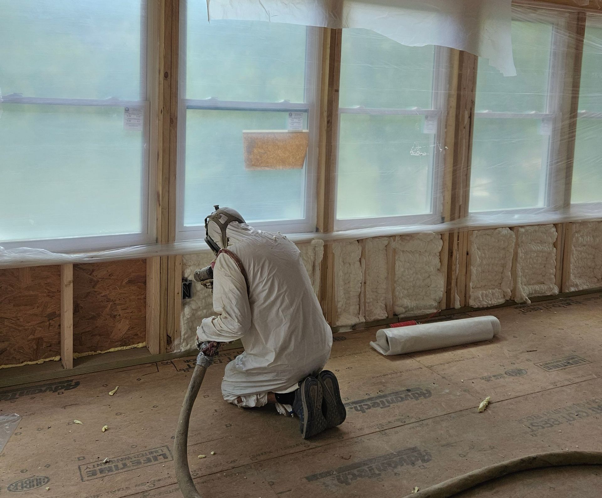 A man in a white suit is spraying insulation on a wall.