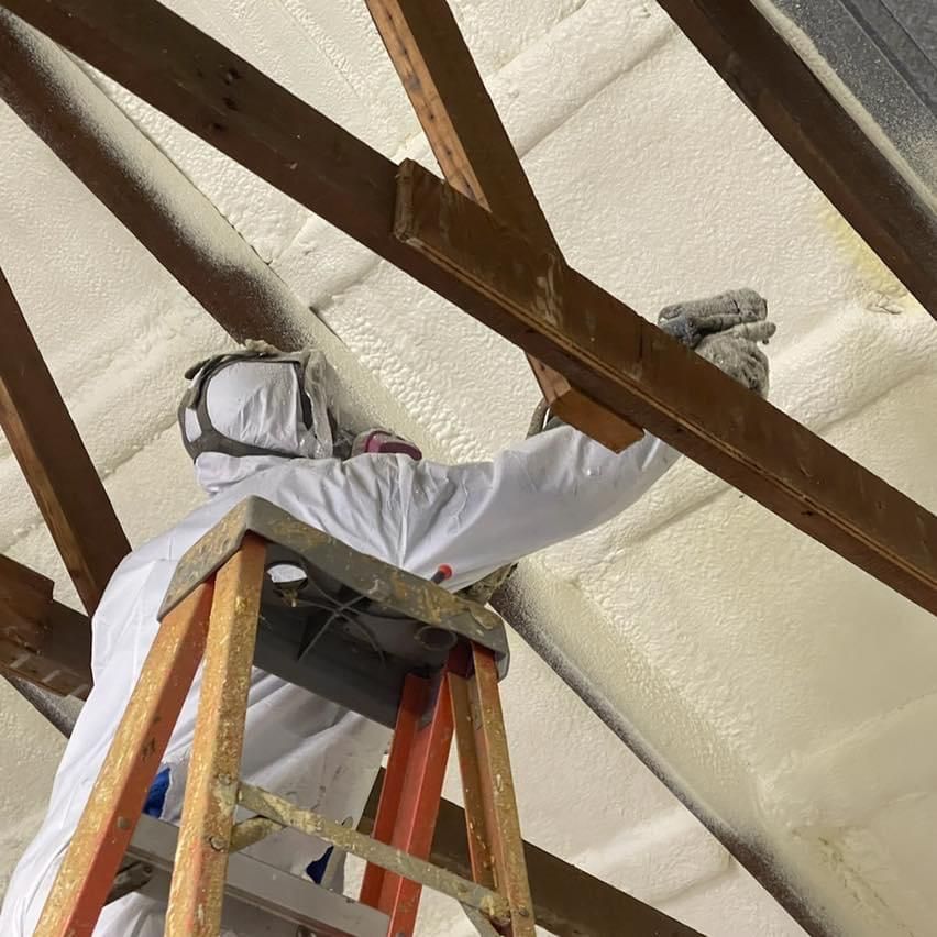 A man on a ladder spraying foam on a ceiling
